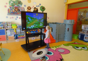 Dziewczynka wskazuje na ekranie mobilnym pszczółkę na ilustracji.